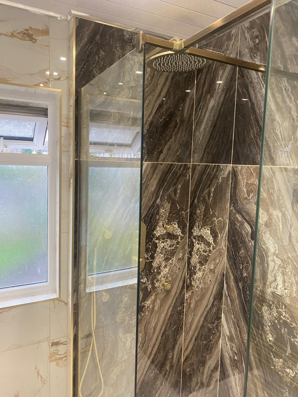 Walk-in shower with brushed gold rainfall head and dark marble feature wall